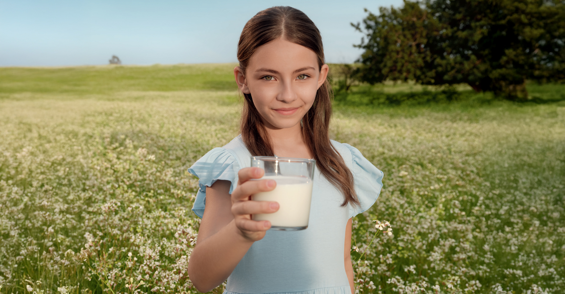 Bambina sarda su campo fiorito porge un bicchiere di latte