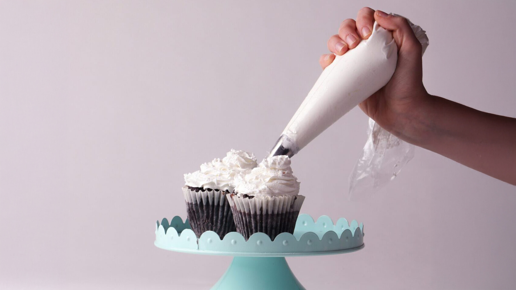 mano che decora con panna due cupcake su alzatina