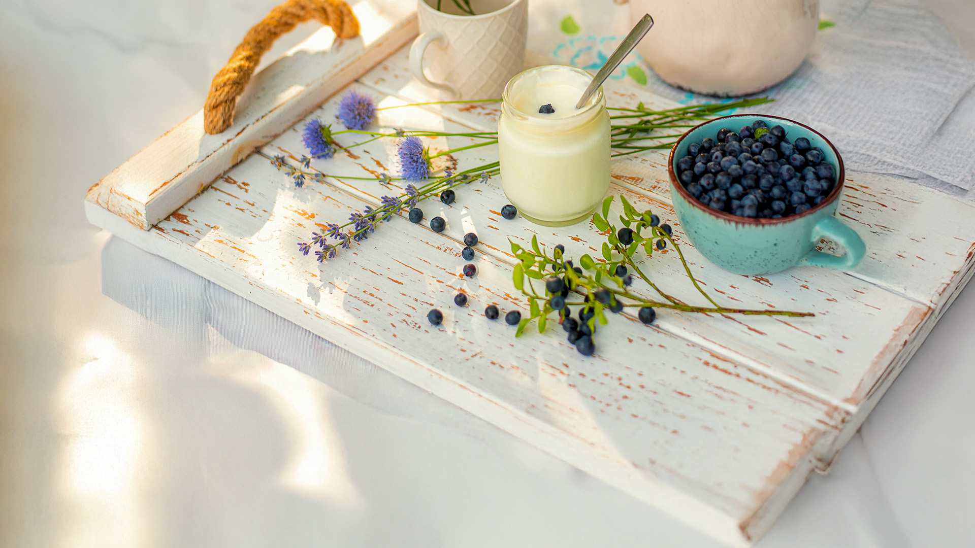 vasetto di yogurt in vetro con ciotola mirtilli su tagliere, sfondo telo bianco bucolico